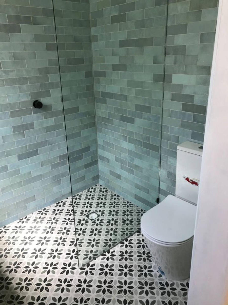 A walk-in shower with a frameless glass panel, sage subway tiles and a patterned tiled floor
