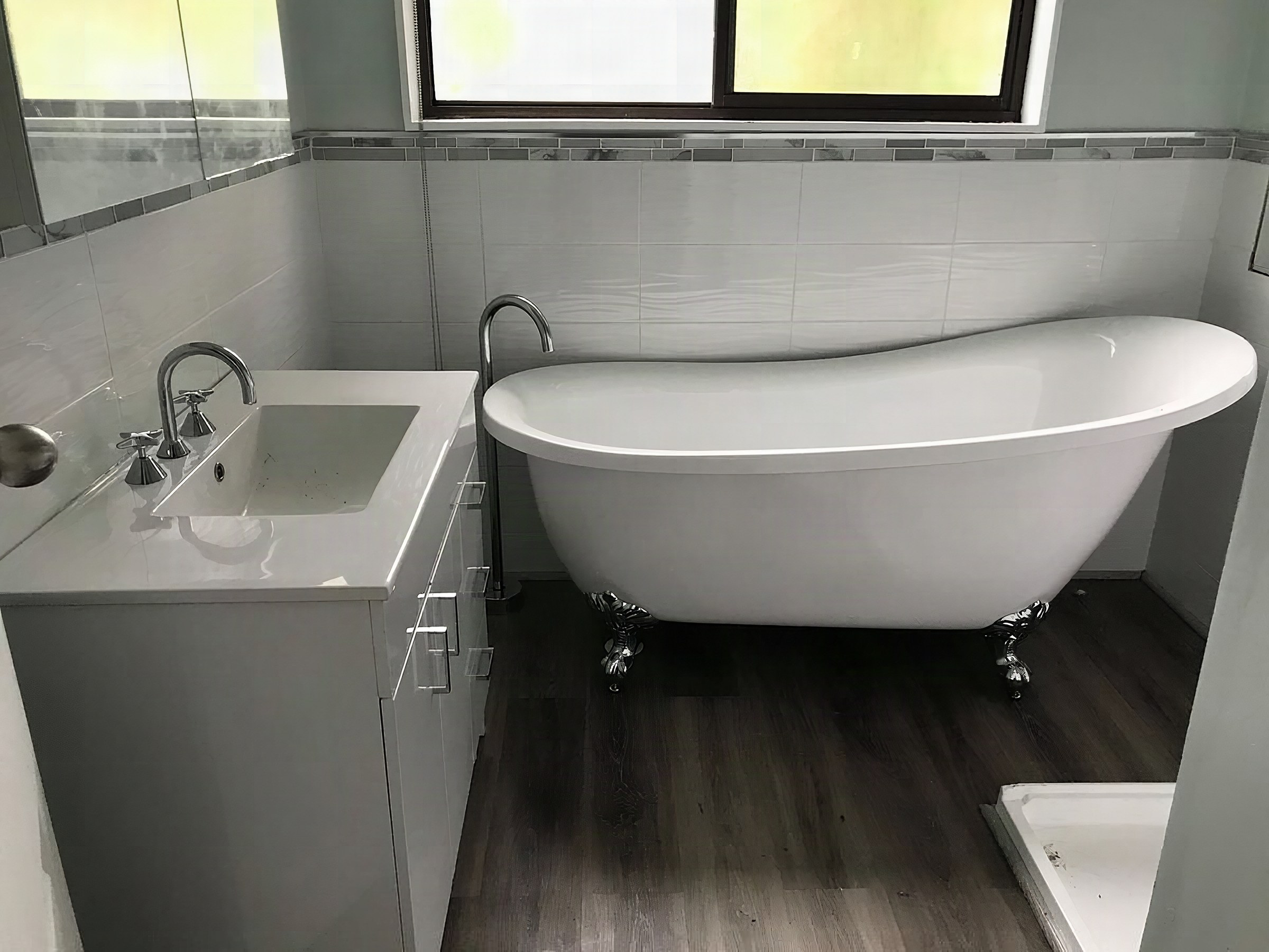 A freestanding slipper bath with a floor-mounted bath filler beside a white vanity