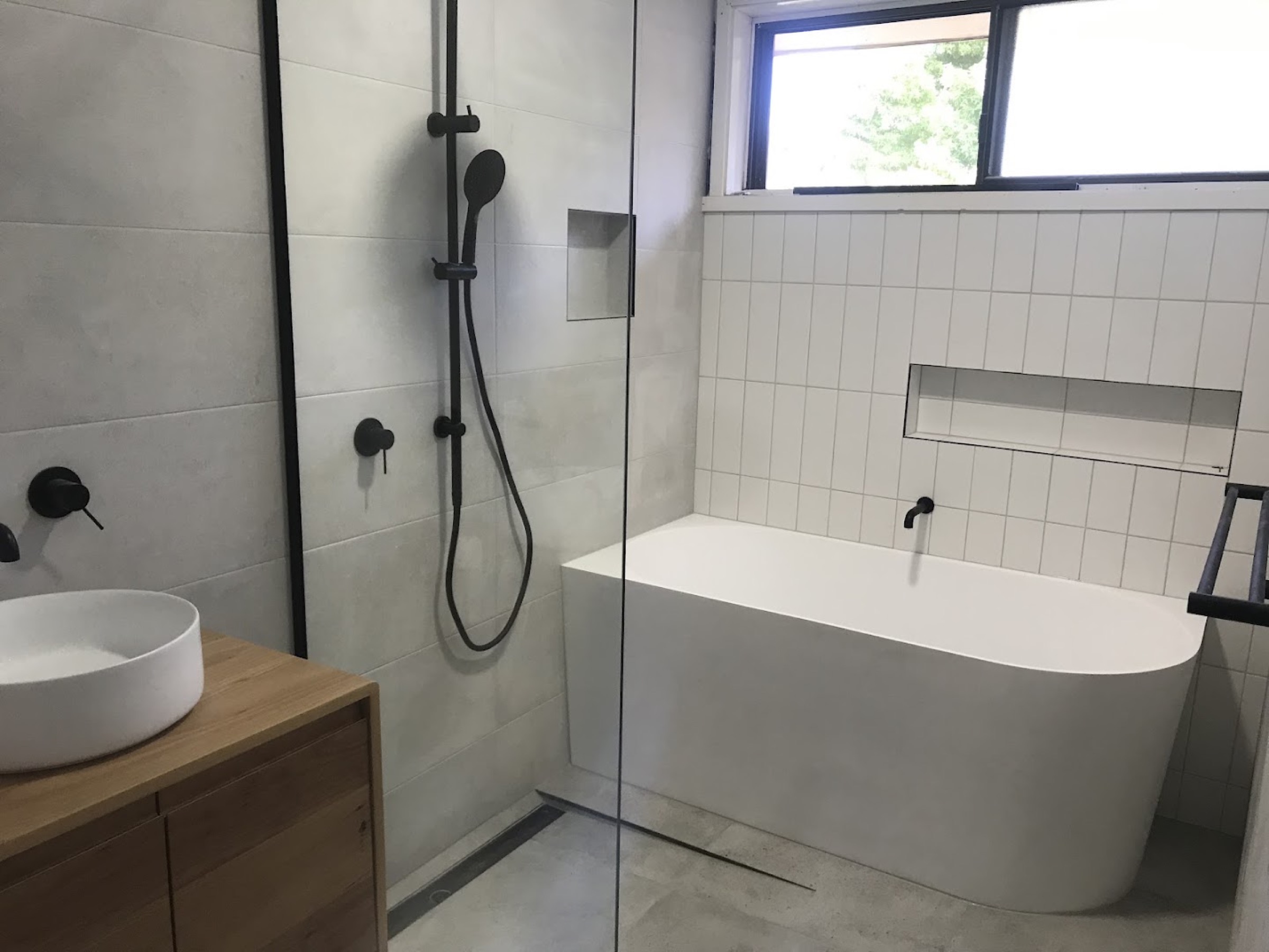 A finished bathroom with a back-to-wall bath, a walk-in shower with black tapware and a timber vanity