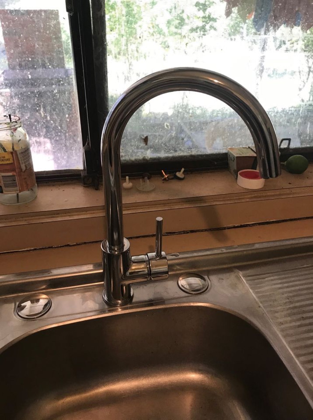 A new chrome gooseneck mixer tap fitted over a stainless steel kitchen sink at a window