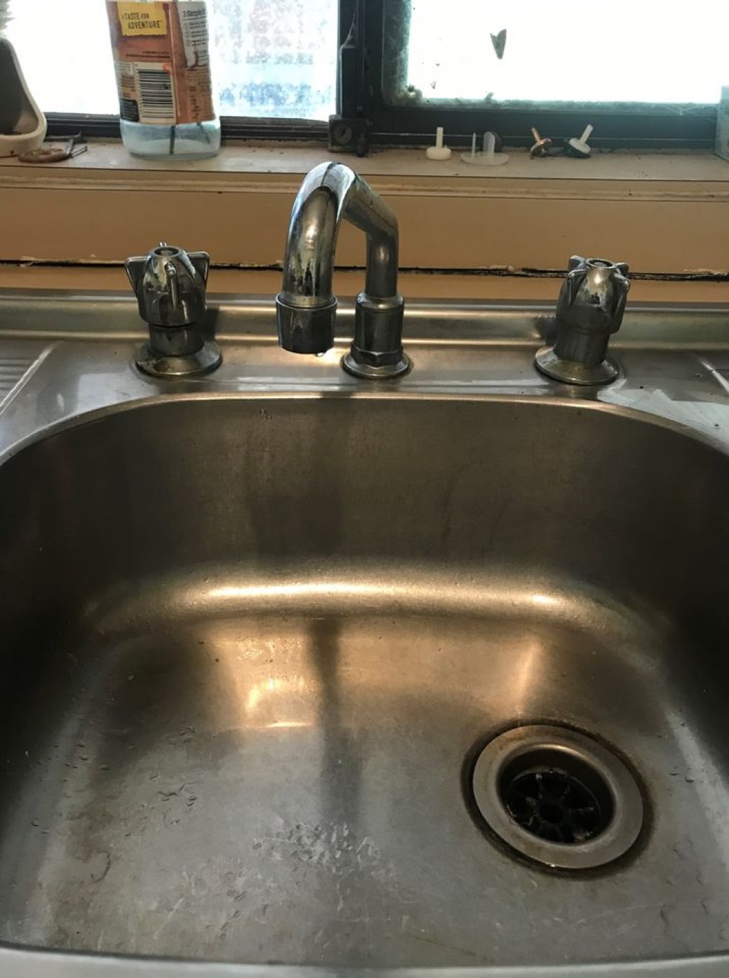 Worn three-piece chrome tapware on a stainless steel kitchen sink