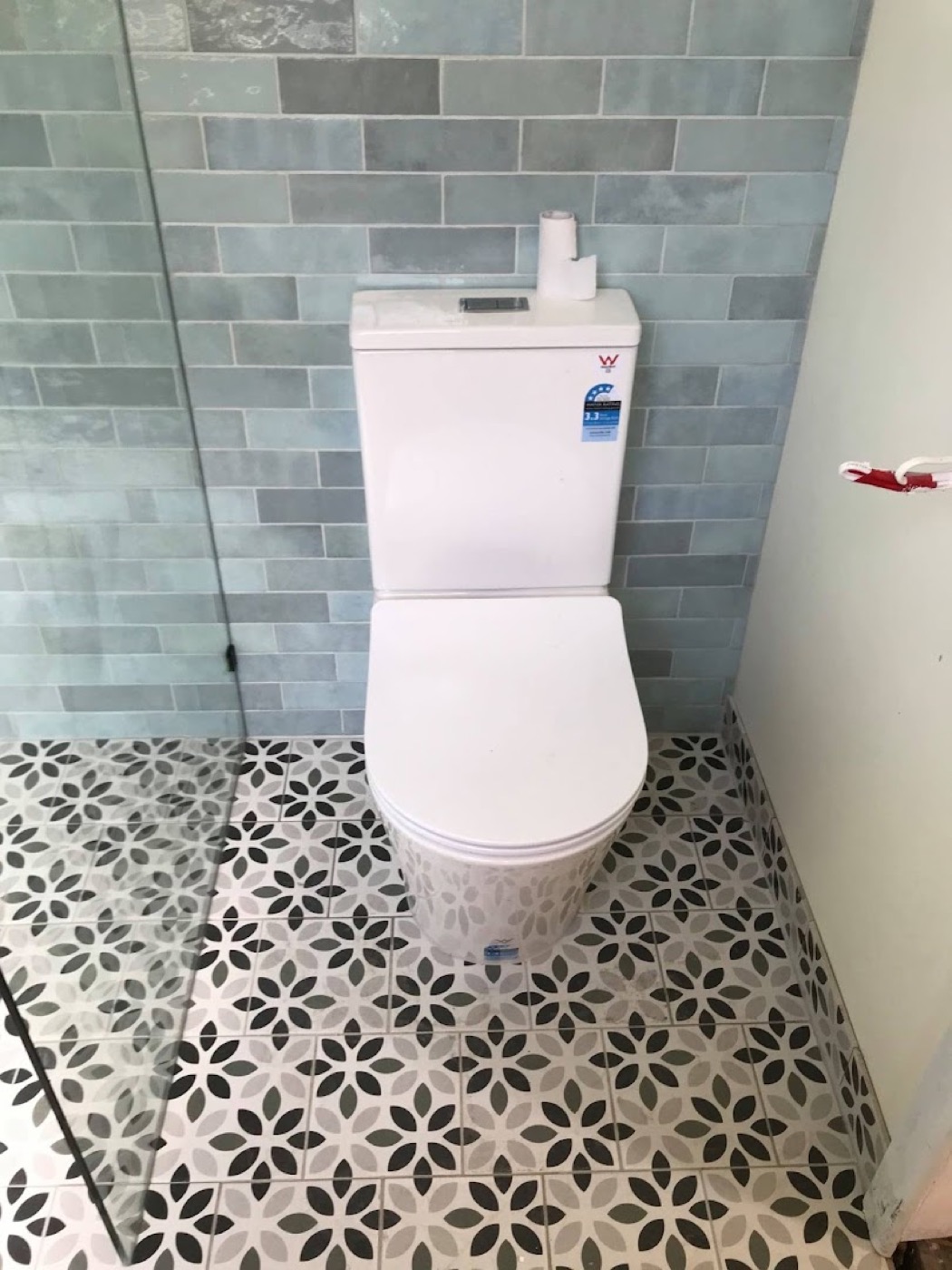 A newly installed close-coupled toilet suite against sage subway tiles on a patterned tiled floor