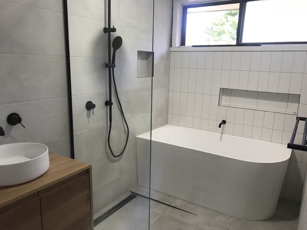 A finished bathroom with a back-to-wall bath, a walk-in shower with black tapware and a timber vanity