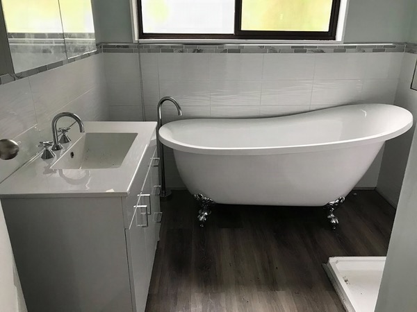 A freestanding slipper bath with a floor-mounted bath filler beside a white vanity
