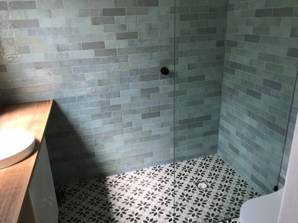A finished shower lined with sage subway tiles above a patterned tiled floor