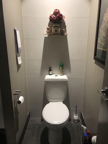 A close-coupled toilet installed in a narrow tiled toilet room