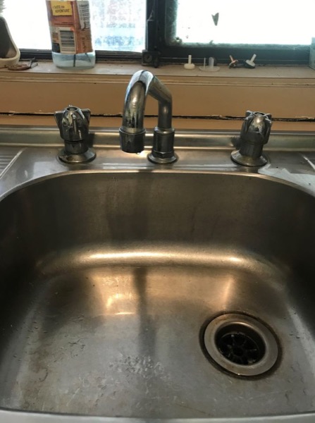 Worn three-piece chrome tapware on a stainless steel kitchen sink