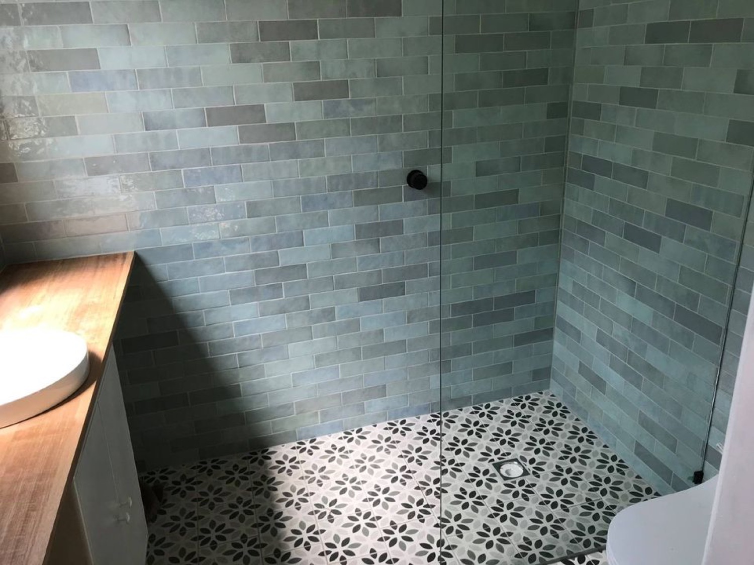 A finished shower lined with sage subway tiles above a patterned tiled floor