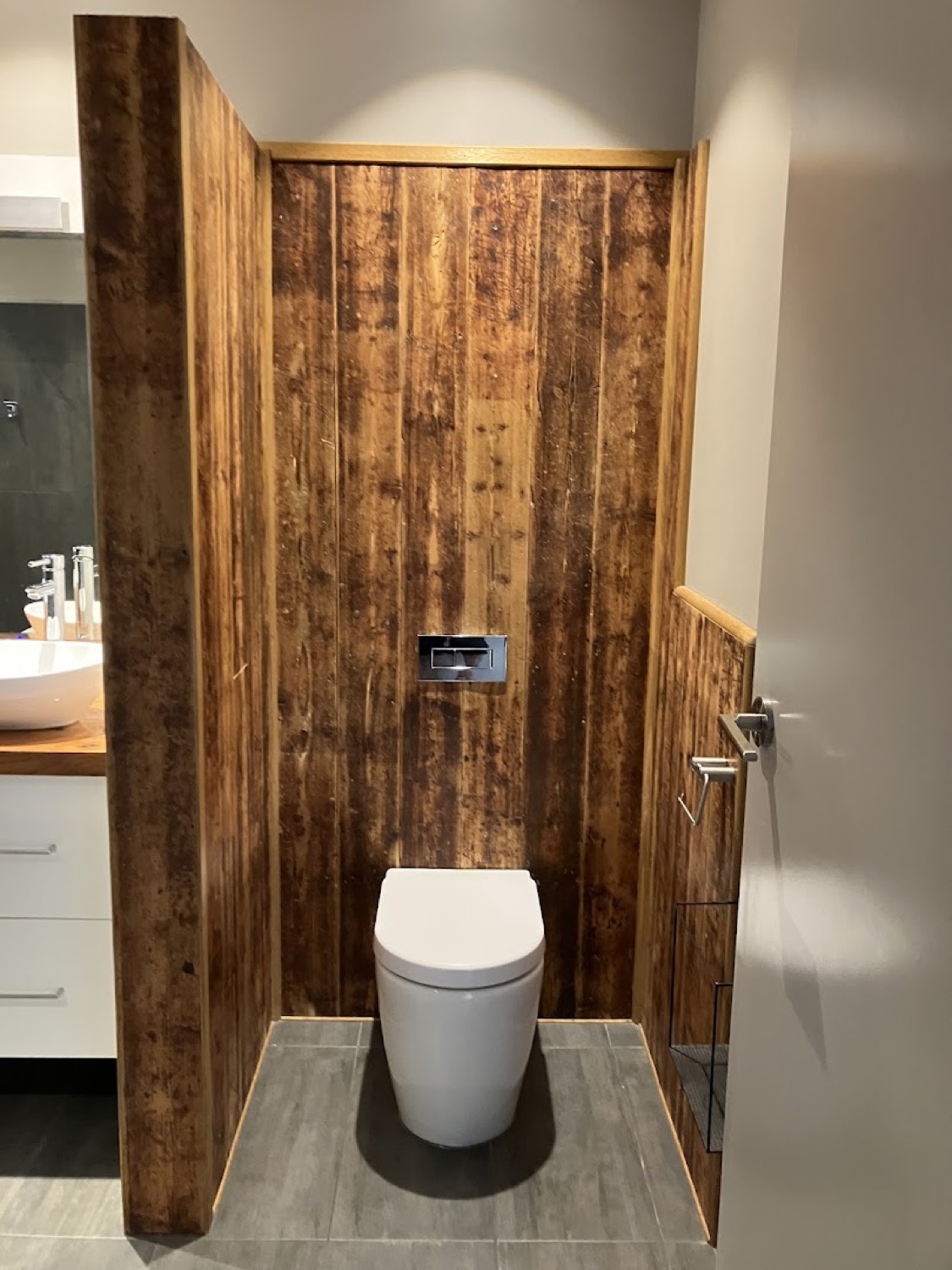 A wall-faced toilet with a concealed cistern set against a recycled timber feature wall